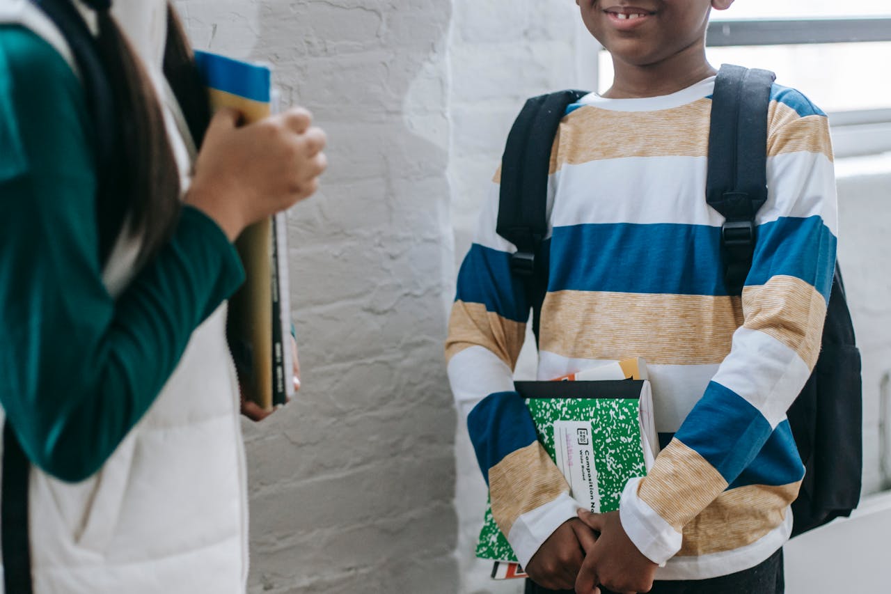 Two schoolchildren smiling and chatting with books in a school hallway, expressing friendship and learning.