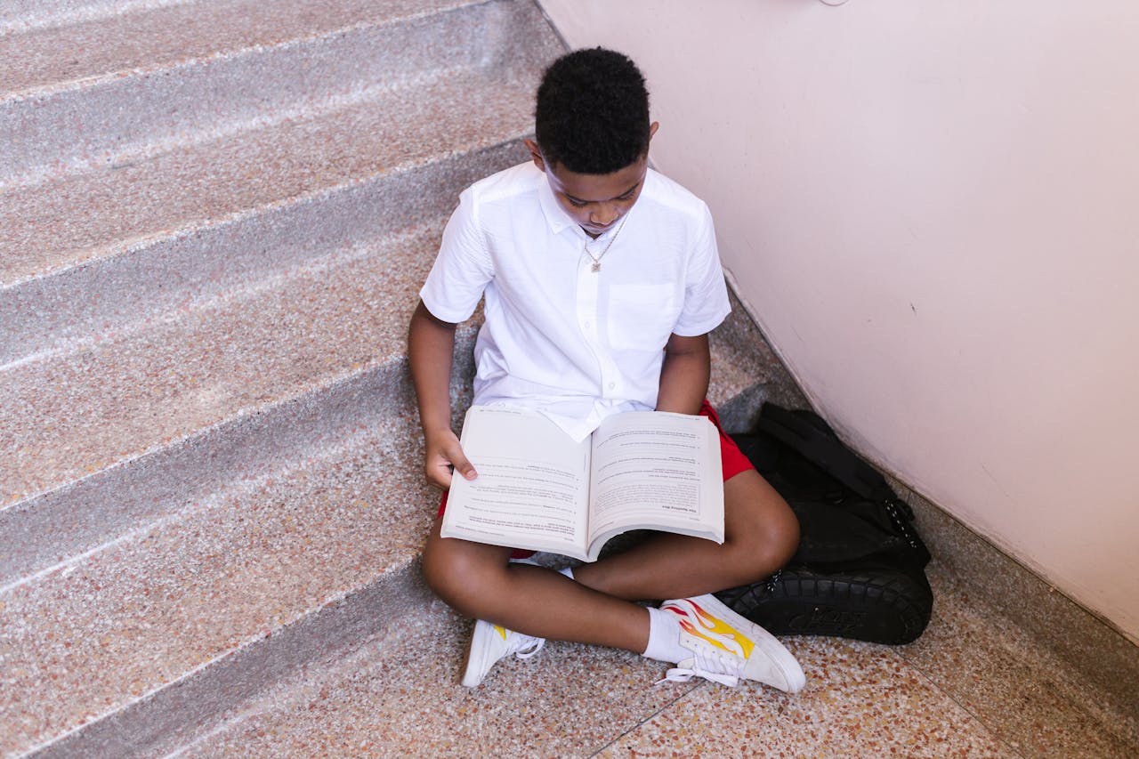 A young boy sitting on stairs with a book, immersed in study.